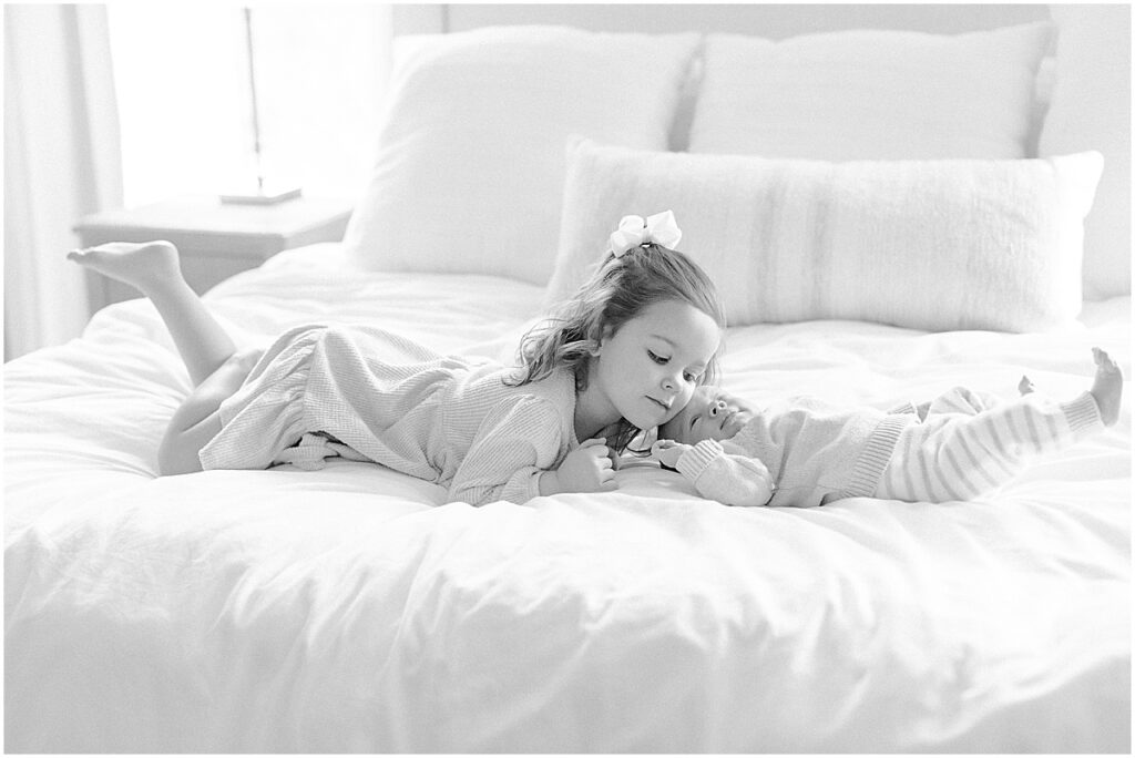 Big sister laying on the bed with baby brother for their Westminster newborn photographer session 